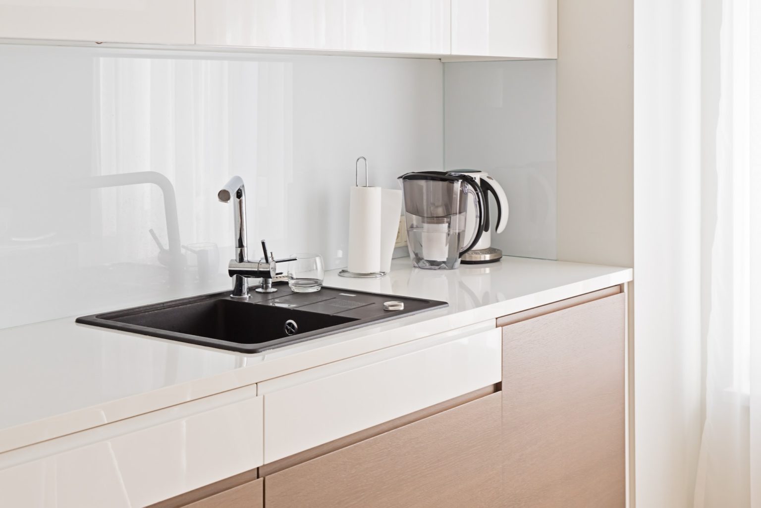 View of modern spacious and light kitchen with dark sink and beige cupboard with copy space